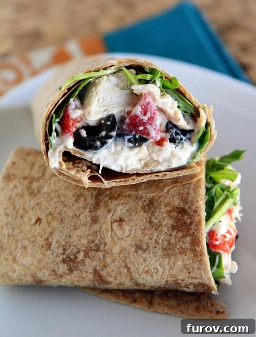 A Mediterranean-filled chicken wrap cut in half on a white plate, showcasing vibrant ingredients.
