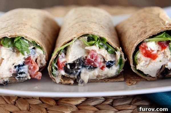 Side view of three Mediterranean-filled chicken wraps neatly arranged on a white plate.