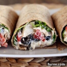 A vibrant Mediterranean chicken wrap halved on a white plate, showcasing fresh ingredients.
