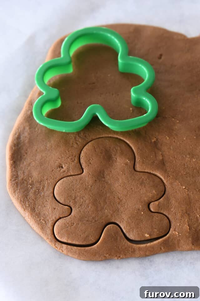 Cutting out gingerbread people with green cookie cutter.
