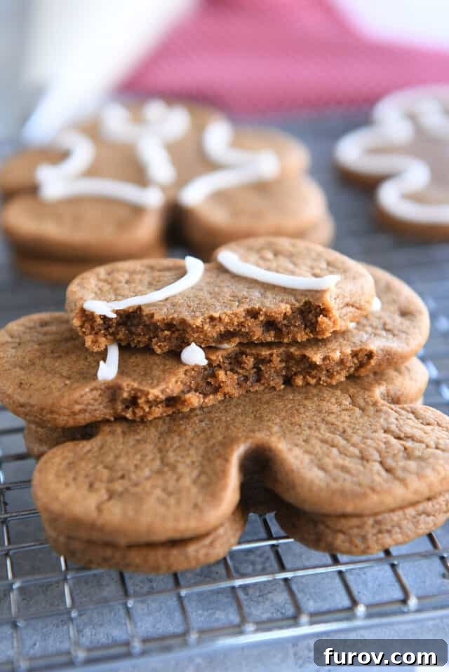Soft and chewy gingerbread cookie broken in half and stacked on two other gingerbread people on wire rack.