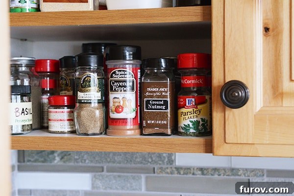 An open kitchen cabinet revealing a neat arrangement of spice jars on shelves.