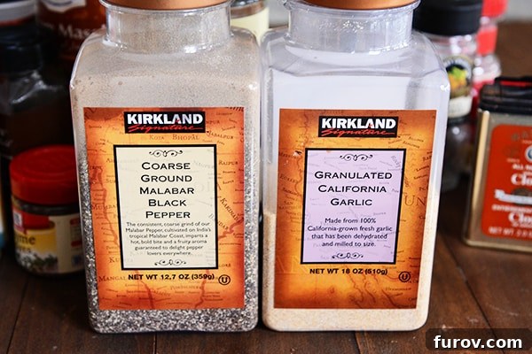 Two large plastic containers of coarse ground black pepper and garlic powder.