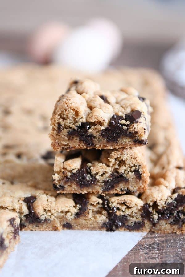 A pair of thick, golden-brown chocolate chip cookie bars, rich with melted chocolate, stacked on a white surface.