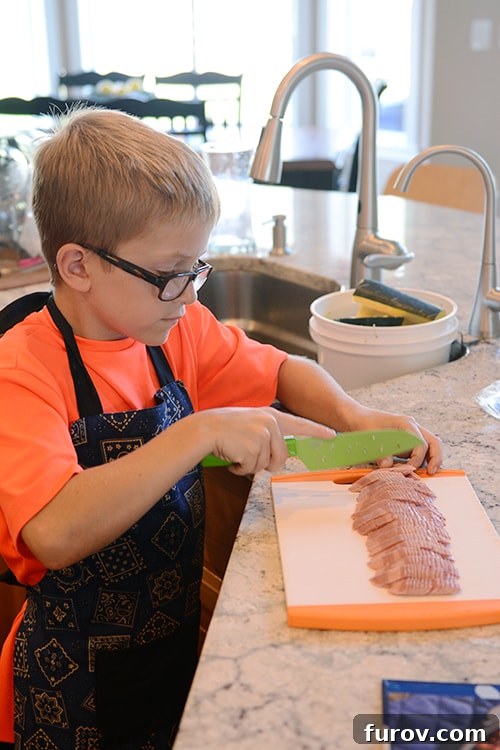 Snapshot Saturday: Mastering Mealtime Mayhem 3 A young boy with a serious expression carefully cutting turkey bacon on a wooden cutting board, focused on his cooking task.
