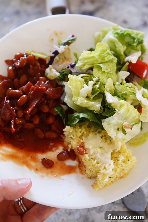 Snapshot Saturday: Mastering Mealtime Mayhem 4 A beautifully plated dinner featuring a golden piece of zucchini cornbread, a scoop of rich BBQ baked beans, and a fresh green salad.
