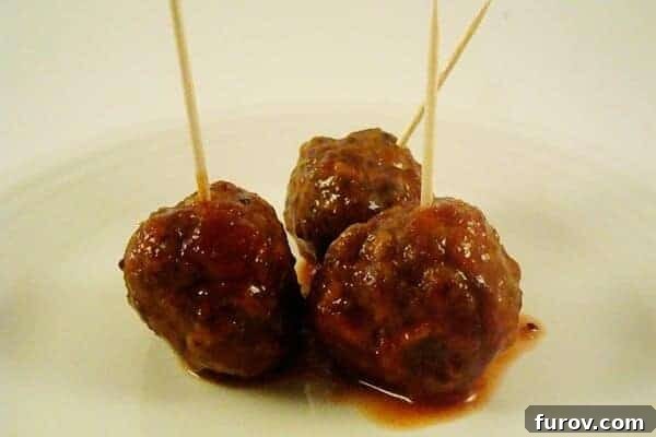 Three saucy meatballs with toothpicks in them on a white plate.