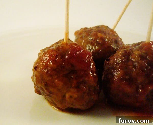 Meatballs covered in sauce with toothpicks in them on a white plate.