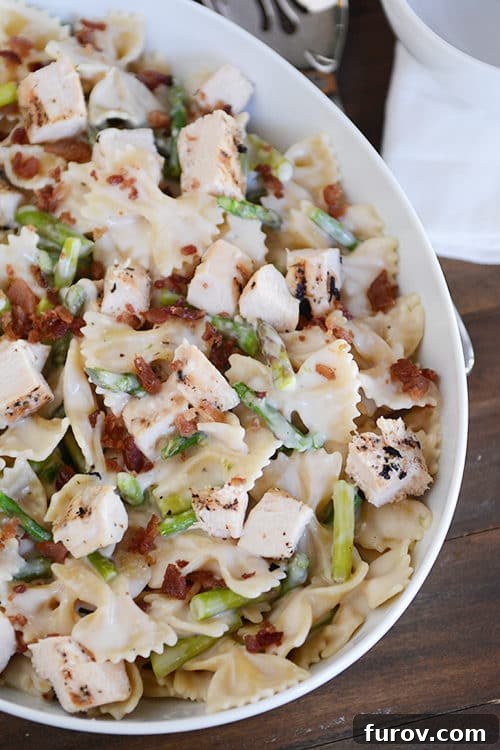 Guilt-Free Bowtie Chicken and Asparagus Alfredo 2 A beautiful white oval bowl filled with creamy bowtie pasta, tender cubed chicken, and vibrant green asparagus, garnished with fresh parsley.