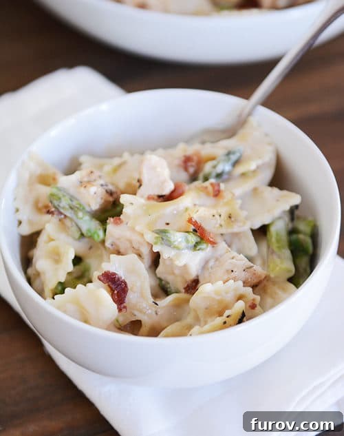 Guilt-Free Bowtie Chicken and Asparagus Alfredo 3 Close-up of a white bowl showcasing creamy bowtie pasta intertwined with bright green chopped asparagus, ready to be enjoyed.