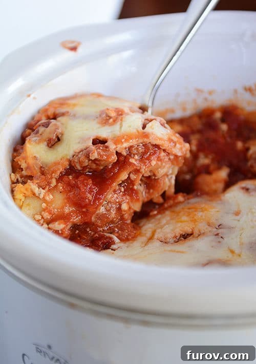 A serving spoon lifting a generous portion of cheesy, saucy lasagna from a slow cooker, showcasing the perfectly cooked noodles and rich texture.