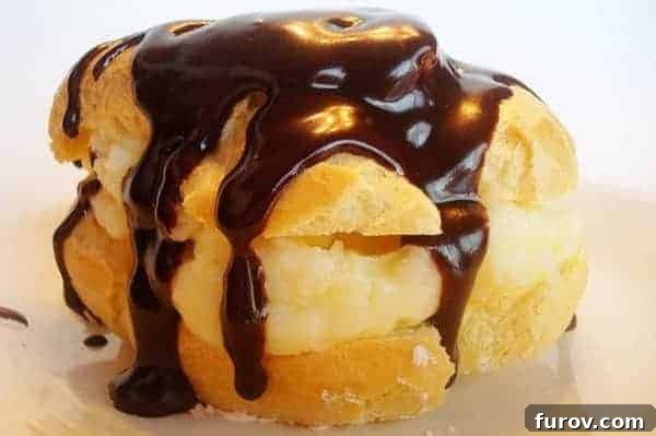 Cream puff drizzled in chocolate on a white plate, showcasing its golden-brown exterior and glaze.