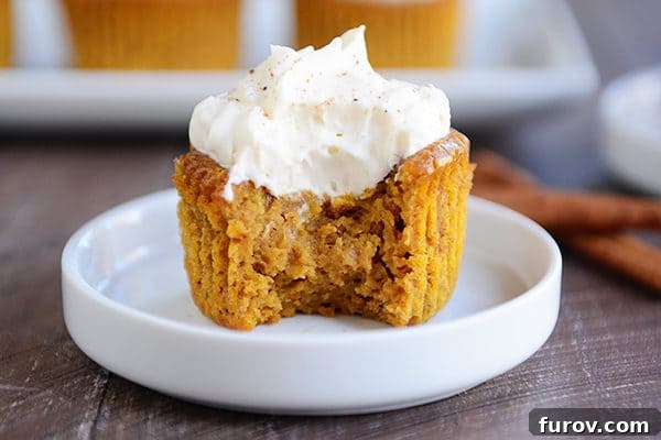 A close-up shot of a crustless pumpkin pie cupcake on a white plate, with a small bite taken out to reveal its creamy, smooth interior. It's generously topped with a dollop of fluffy whipped cream, inviting a taste.