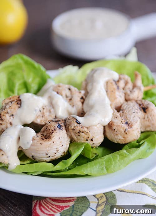 Zesty Grilled Chicken Skewers with Creamy Yogurt-Hummus Dip 2 Hummus sauce drizzled grilled chicken skewers laying on lettuce leaves.
