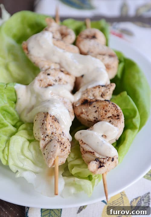 Zesty Grilled Chicken Skewers with Creamy Yogurt-Hummus Dip 3 Two grilled chicken skewers drizzled with a yogurt hummus sauce.