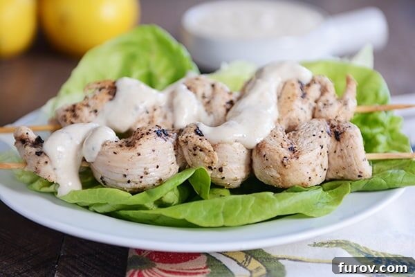 Zesty Grilled Chicken Skewers with Creamy Yogurt-Hummus Dip 4 Grilled chicken skewers laying on lettuce leaves and drizzled with sauce.