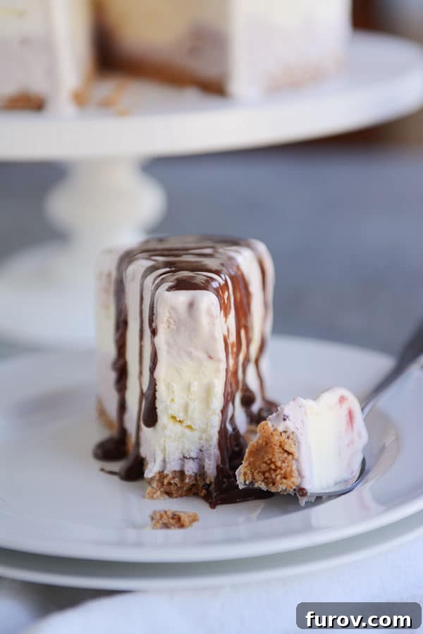 A slice of ice cream cake topped with chocolate syrup on a white plate with one bite of it on a fork next to it.