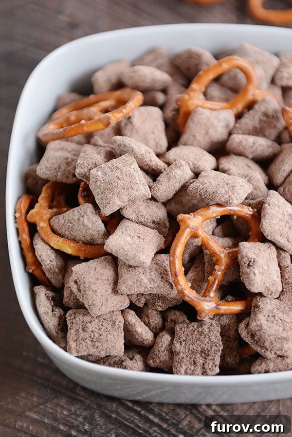 Fudgy Brownie Batter Buddies 2 Top view of a white bowl overflowing with chocolate muddy buddies and crunchy pretzels.
