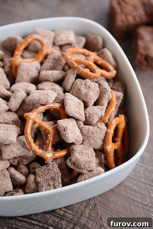 Fudgy Brownie Batter Buddies 4 A vibrant white bowl generously filled with irresistible chocolate muddy buddies and crispy pretzels.