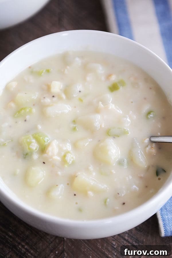 Our Go-To New England Clam Chowder 3 Top-down view of a steaming bowl of creamy New England clam chowder, garnished with fresh herbs, showcasing its rich texture and chunks of vegetables.