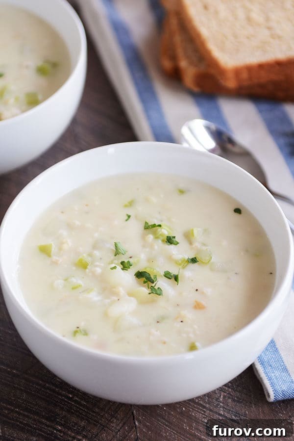Our Go-To New England Clam Chowder 5 A generous serving of New England clam chowder in a white bowl, artfully garnished with fresh parsley.