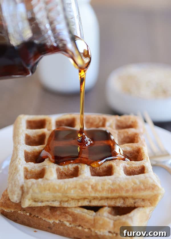 Syrup being poured over two thick Belgian waffles, highlighting the golden-brown crispness and fluffy interior.