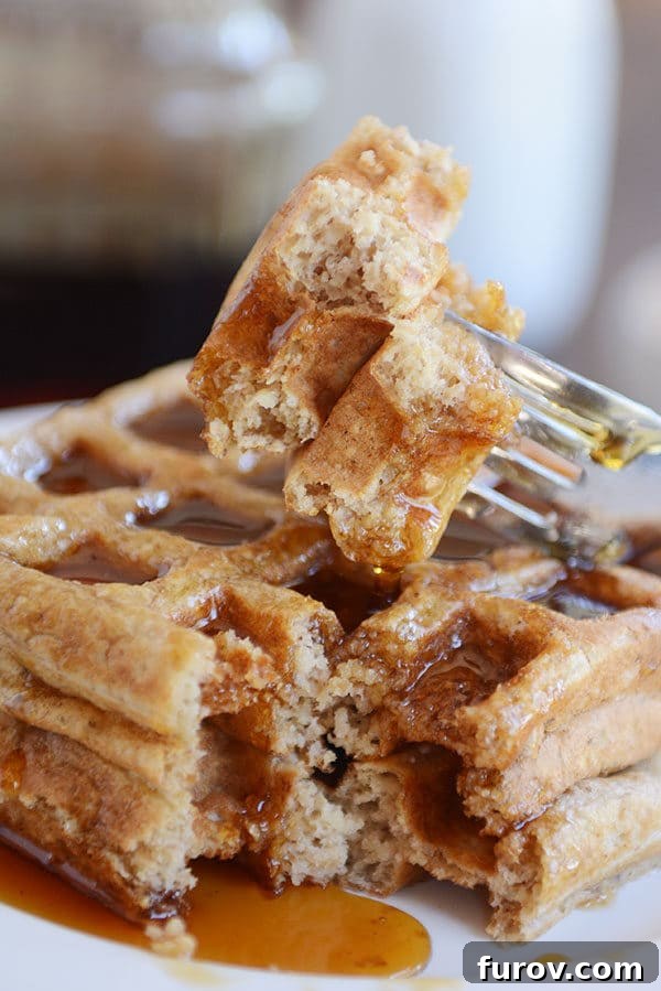 A fork taking a bite out of two stacked syrupy waffles, showcasing their tender texture.