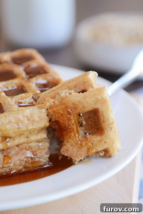 A fork taking a bite out of two thick syrupy waffles on a white plate, highlighting their soft texture.