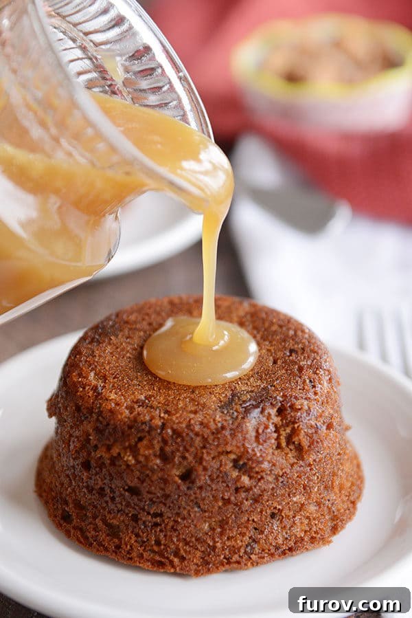 A small cake on a white plate, with sticky toffee sauce being poured over the top. 