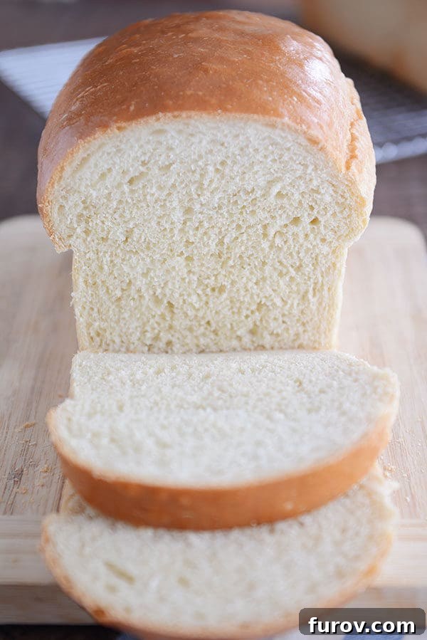 A golden-brown loaf of homemade white sandwich bread, with two inviting slices cut and placed in front.