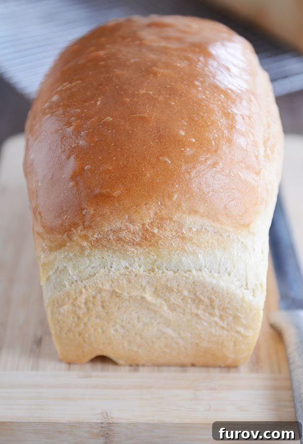 A freshly baked loaf of homemade white bread resting on a rustic wooden cutting board, ready to be sliced.