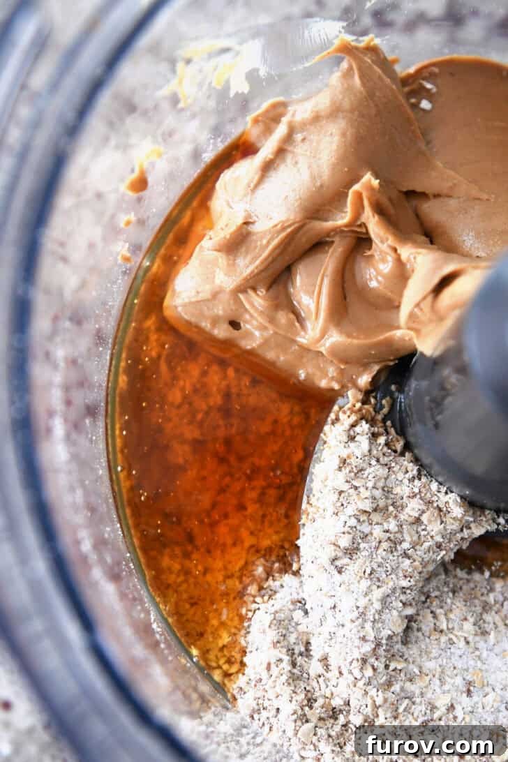 Top-down view of peanut butter, honey, and oats ready to be processed in a food processor.