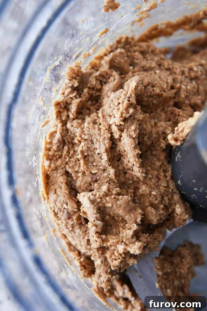 Top-down view of a partially mixed peanut butter and oat mixture in a food processor, forming a cohesive dough.