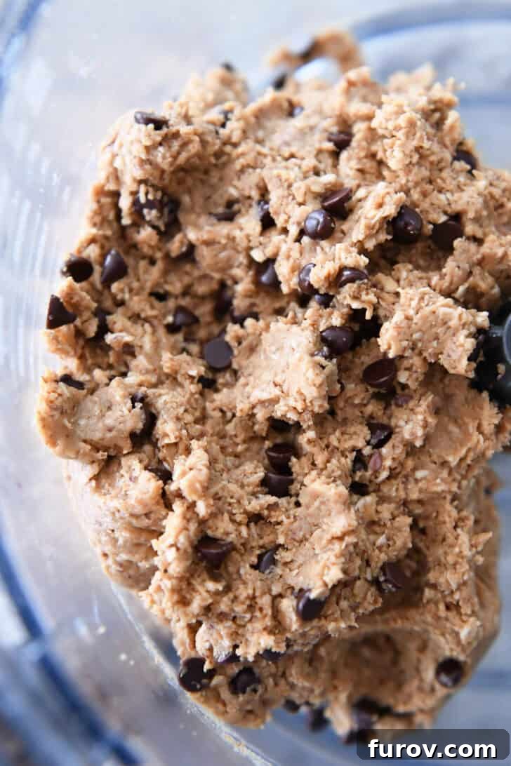 Top-down view of peanut butter oat dough with mini chocolate chips, ready for final mixing in a food processor.