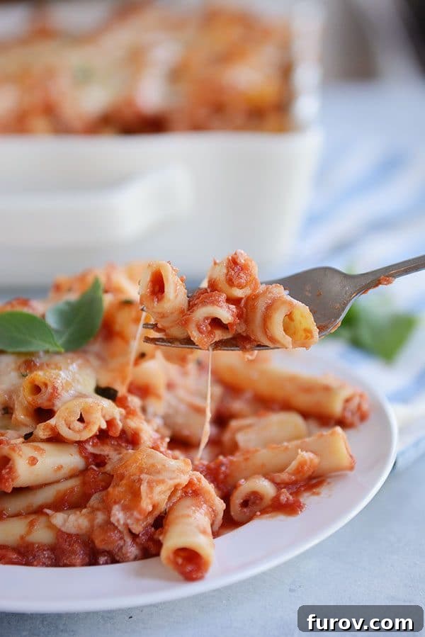 Dondurucu Dostu Fırında Peynirli Ziti 3 A fork taking a bite of cheesy red sauce baked ziti off of a white plate.