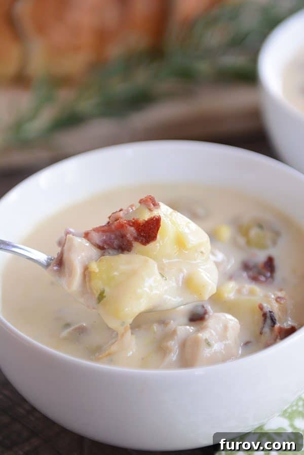 A beautifully styled bowl of creamy potato soup, garnished with crispy bacon and fresh sage, with a rustic loaf of bread in the background.