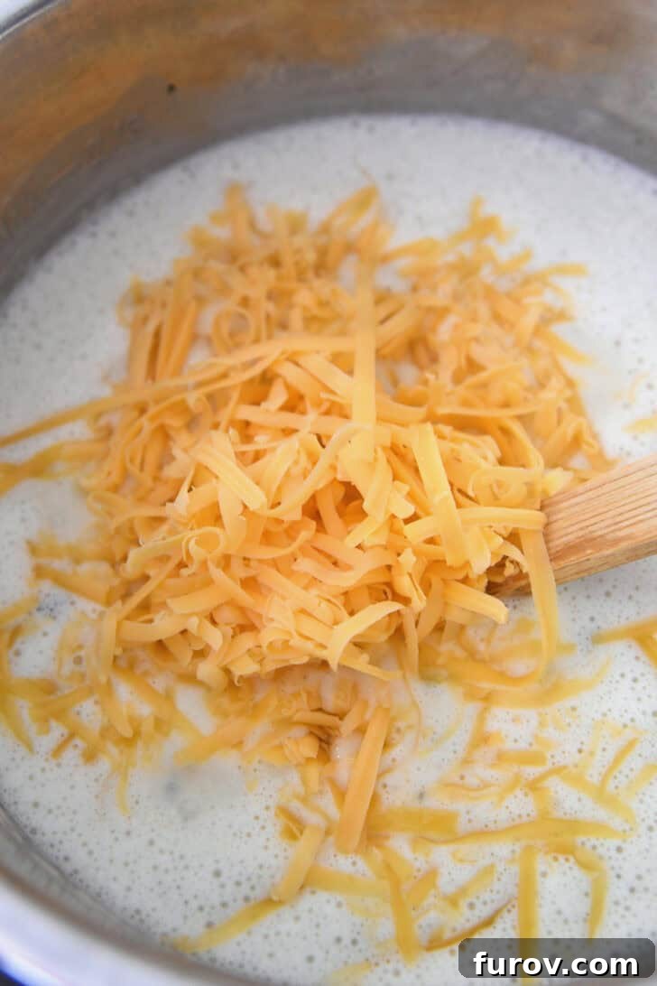 Shredded sharp cheddar cheese being added to a simmering, creamy potato soup in an Instant Pot.