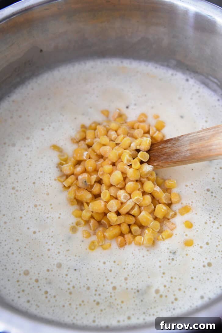 Frozen corn kernels being stirred into a rich and creamy Instant Pot potato soup.