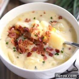 A comforting white bowl of creamy potato soup, garnished with crispy bacon and fresh chives.