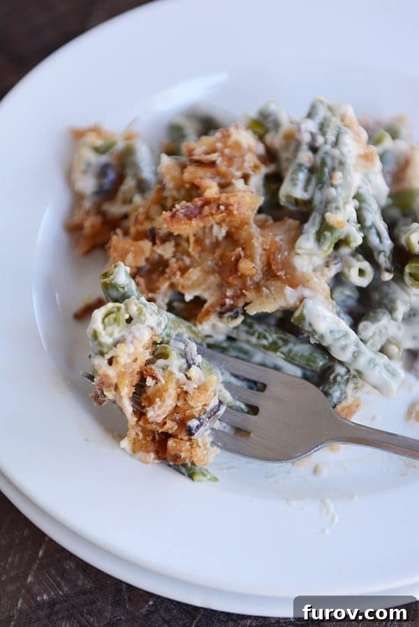 A large helping of green bean casserole topped with crunchy topping on a white plate, showcasing its rich texture.