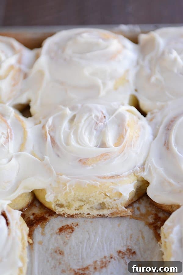 A pan of frosted cinnamon rolls with one taken out, ready to be enjoyed. The frosting is generously drizzled over them.