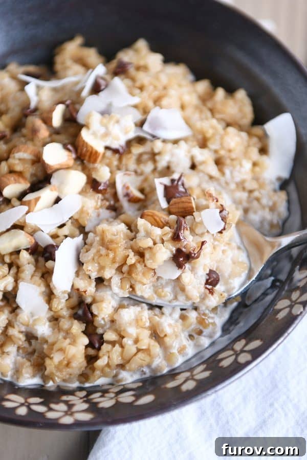 Decadent Instant Pot Slow Cooker Coconut Steel Cut Oatmeal 2 A brown bowl filled with creamy coconut milk steel cut oats, garnished with chocolate chips, sliced almonds, and shredded coconut. The textures are rich and inviting.