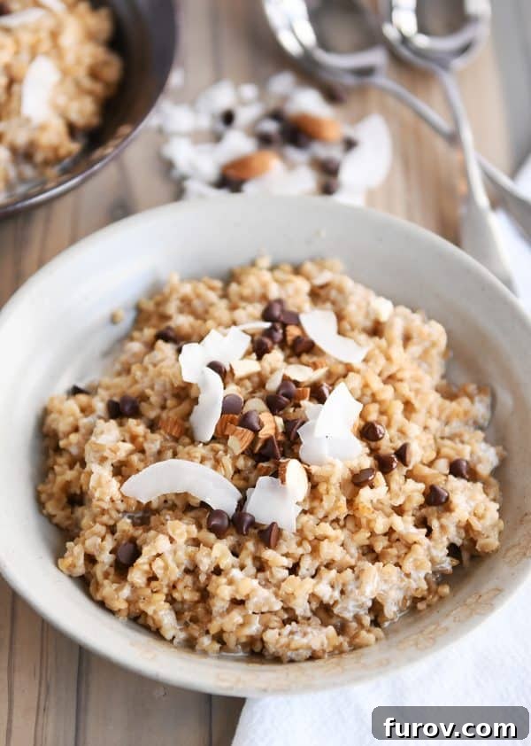 Decadent Instant Pot Slow Cooker Coconut Steel Cut Oatmeal 3 A white bowl showcasing creamy coconut milk steel cut oats, adorned with mini chocolate chips, shredded coconut, and chopped almonds. The presentation is elegant and appealing.