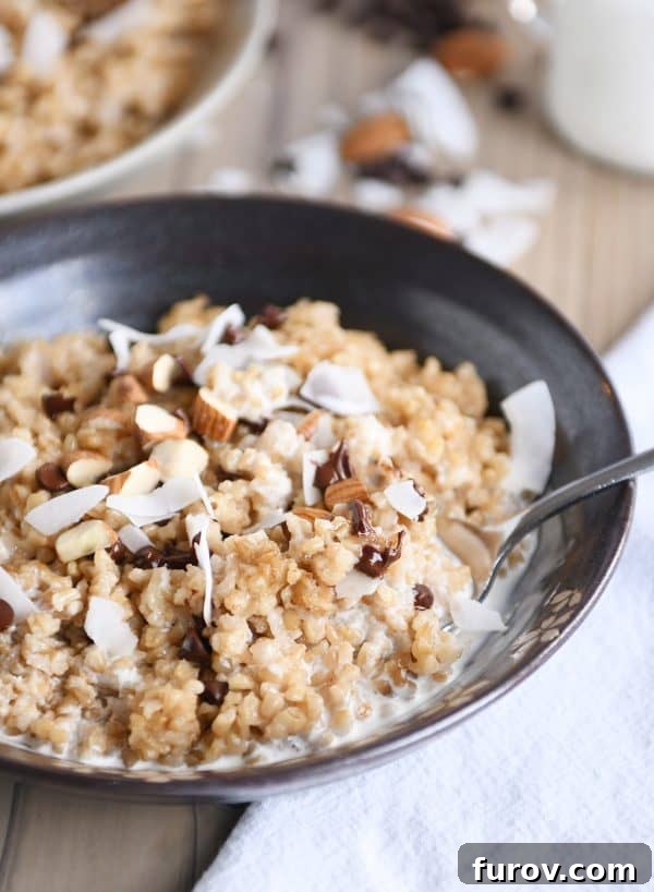 Decadent Instant Pot Slow Cooker Coconut Steel Cut Oatmeal 4 A close-up of a brown bowl of creamy coconut milk steel cut oats, generously topped with melted chocolate chips, crunchy almonds, and delicate coconut flakes. The image highlights the inviting texture and delicious toppings.