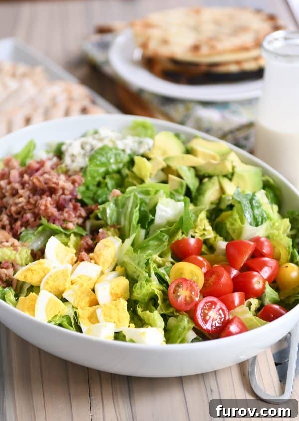Chargrilled Chicken Cobb Salad 3 Grilled chicken cobb salad in a white bowl, showcasing layers of crisp lettuce, juicy tomatoes, hard-boiled eggs, crumbled bacon, and vibrant blue cheese.