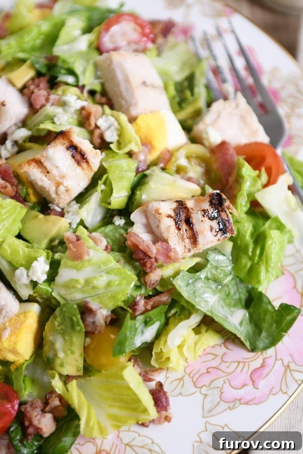 Chargrilled Chicken Cobb Salad 4 A vibrant Grilled Chicken Cobb Salad artfully arranged on a white plate with delicate pink flowers, highlighting its fresh and inviting appearance.
