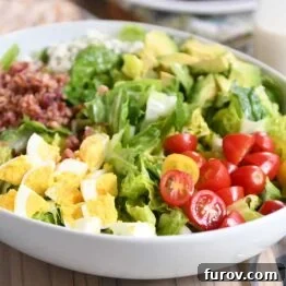 Grilled chicken cobb salad in white bowl with lettuce, tomatoes, eggs, bacon and blue cheese, perfectly composed and ready to serve.