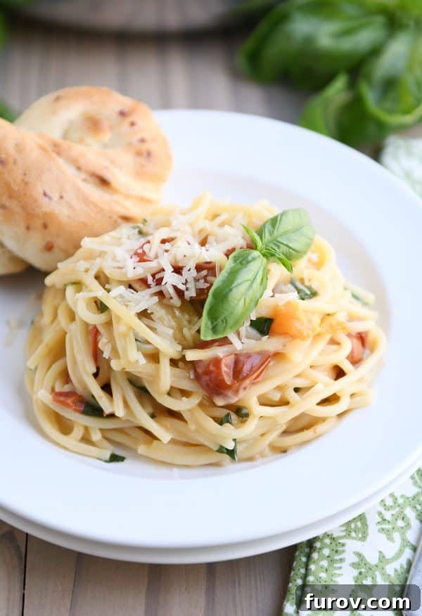 A serving of creamy tomato basil pasta on a white plate, accompanied by a parmesan breadstick.
