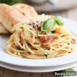 One pot creamy tomato basil pasta on white plate with parmesan breadstick.