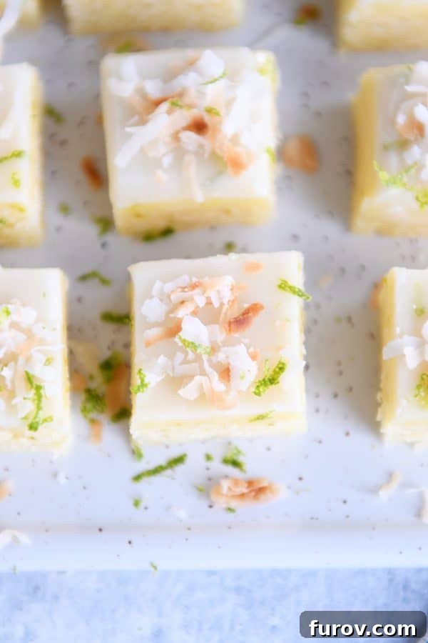 An overhead view of toasted coconut lime bars on a white platter, showcasing their uniform shape and generous topping of toasted coconut.